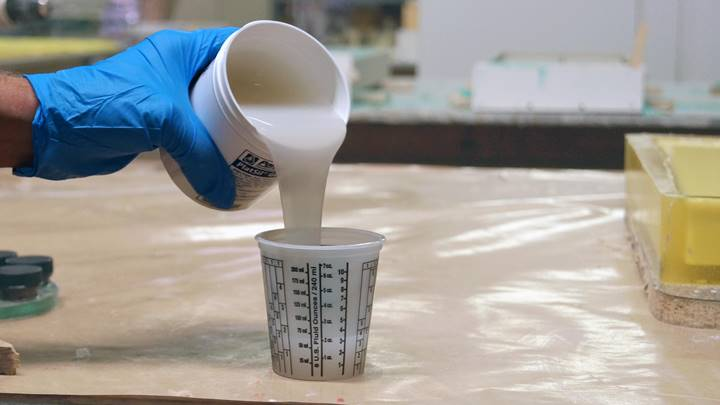 Worker pouring liquid platinum-cured silicone into a measuring cup in a workshop setting